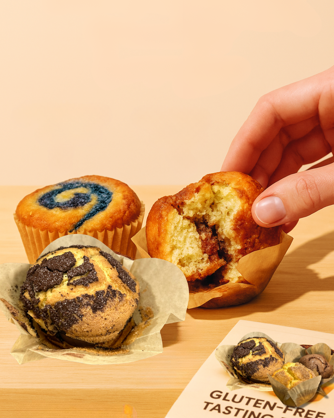 Three muffins on a wooden surface with a hand reaching for one of them.